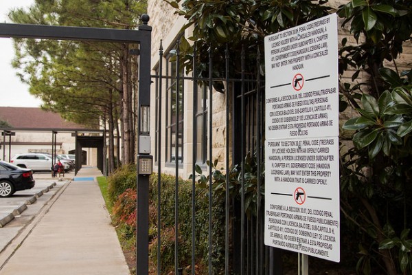 A 30.06 sign stating school gun policy is posted on a gate to campus.