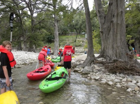 Freshmen trudge their kayaks along shallow water and rocky paths.