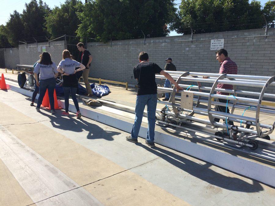 Adviser and physics teacher Nolan Harris, far right, accompanies the team as they place their pod on the track. On the far left is the pod pusher.