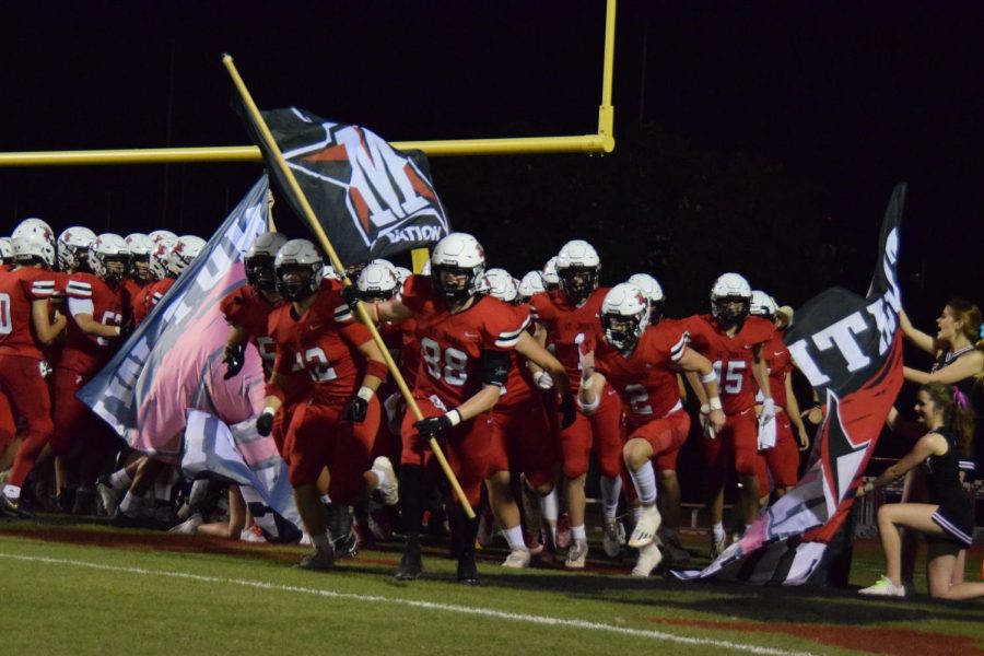 The Maverick football team bursts through the banner, ready to compete and dominate the field. 