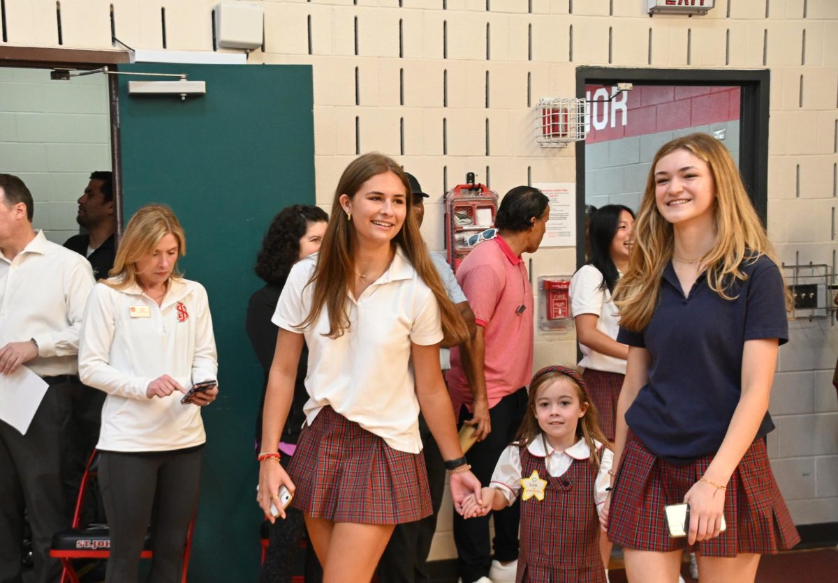 Seniors Mia Hirshfeld and Georgia Andrews escort kindergarten student Lila Thompson to her spot at the all-school assembly.