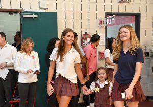 Seniors Mia Hirshfeld and Georgia Andrews escort kindergarten student Lila Thompson to her spot at the all-school assembly.