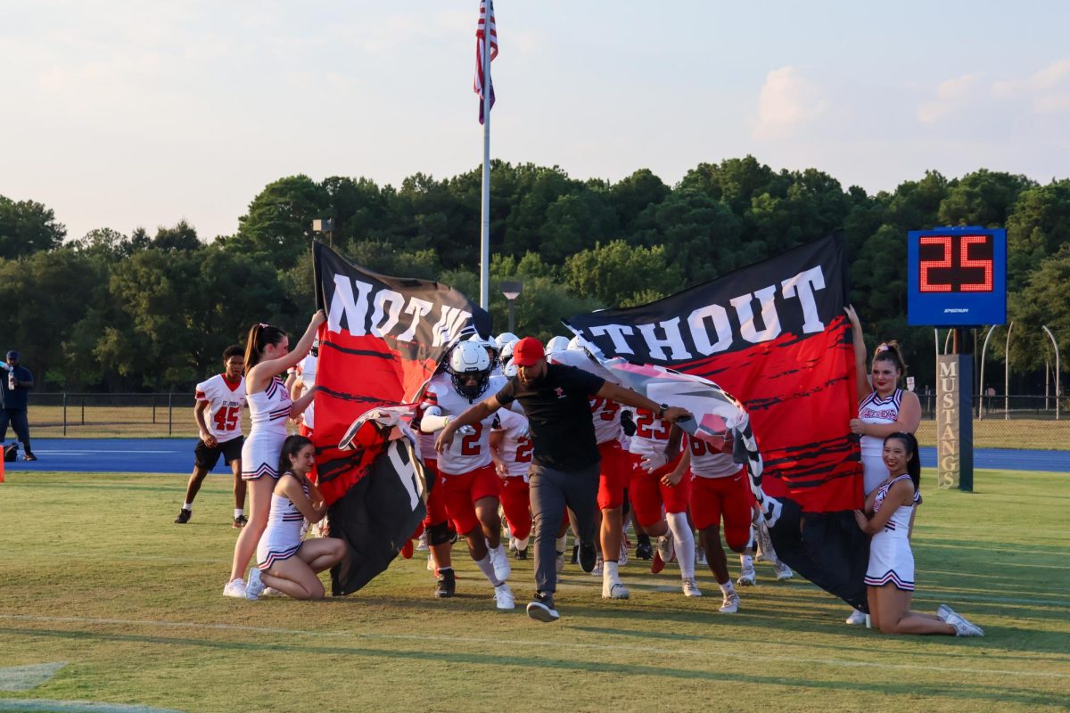 Coach Brian Gobert guides the football team as they burst through the Mavericks banner bearing the school motto, Not Without Honor. 